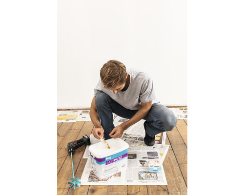 Un homme ouvre un paquet d''enduit prêt à l''emploi de la marque Knauf pour effectuer des travaux de réparation.