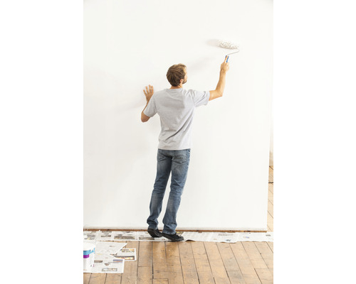 Homme peignant un mur avec un rouleau à peinture dans une pièce lumineuse
