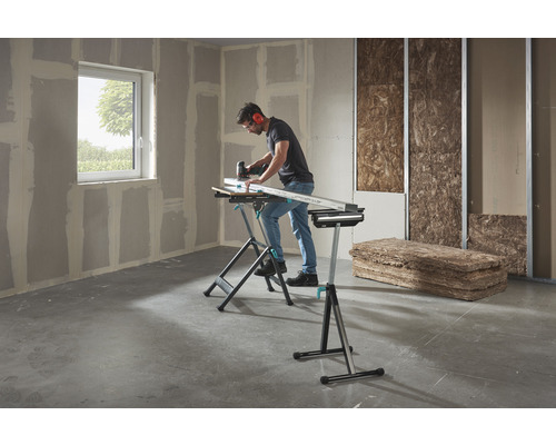 Un homme travaille avec une scie sauteuse sur une pièce sur un établi Wolfcraft dans une pièce avec des plaques de plâtre et des matériaux isolants.