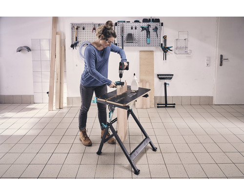 Une femme travaille avec une perceuse sur un établi dans un atelier.