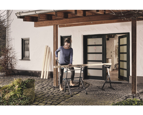 Une femme scie du bois sur un établi pliant à l''extérieur.
