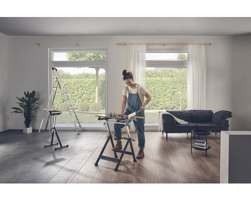 Une femme scie du bois sur un établi dans une pièce lumineuse