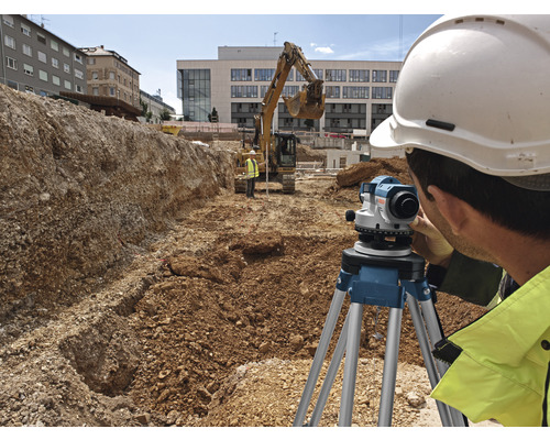 Ein Bauarbeiter mit Helm bedient ein Nivelliergerät auf einer Baustelle.