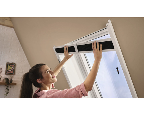 Frau montiert ein Verdunkelungsrollo an einem Dachfenster