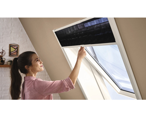 Frau bedient Dachfensterrollo im Dachzimmer