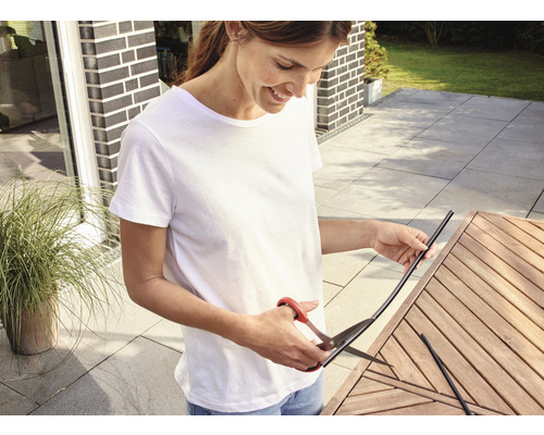 Frau schneidet Kantenumleimer mit einer Schere auf einem Holztisch im Freien