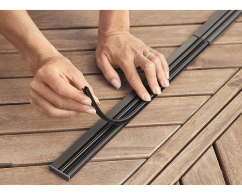 Person setzt Dichtungsprofil in eine Metallschiene auf einem Holztisch