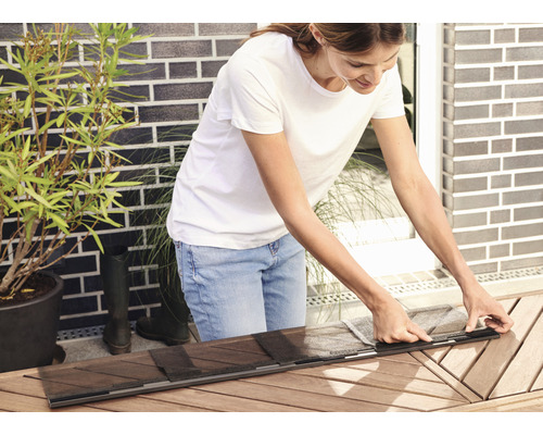 Frau montiert Insektenschutzgitter auf Holztisch im Freien