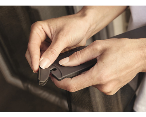 Zwei Hände befestigen ein Insektenschutzgitter mit einem Werkzeug.