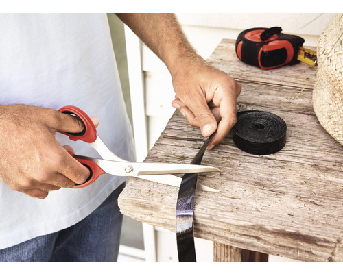 Eine Person schneidet ein schwarzes Kunststoffband mit einer Schere auf einem Holztisch.