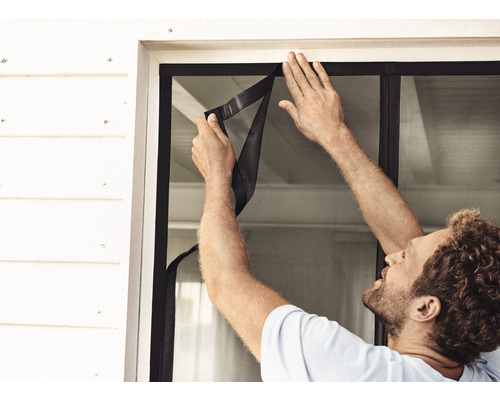 Mann installiert ein Fliegengitter am Fenster