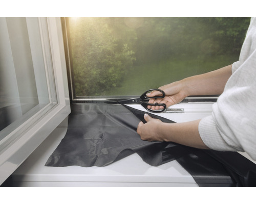 Zuschneiden einer Verdunkelungsfolie für Fenster mit einer Schere.