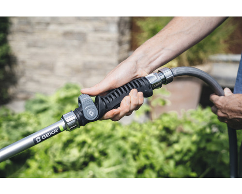 Une personne tient un pulvérisateur de jardin de la marque Geka sur un tuyau d''arrosage.