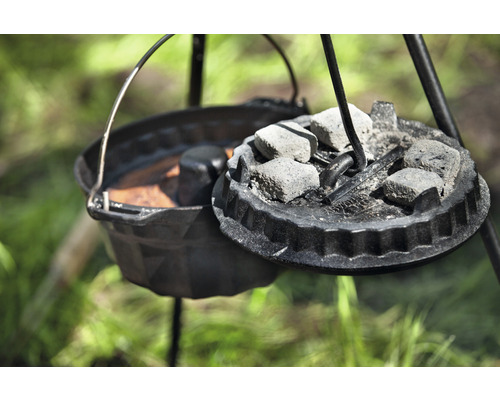 Gusseiserner Dutch Oven mit Deckel und Briketts auf einem Dreibein