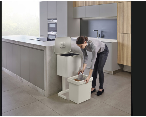 Une femme jette une bouteille en verre dans un système de tri des déchets dans la cuisine.