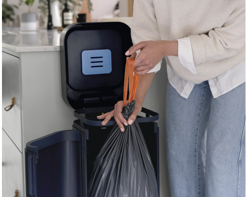 Une personne jette des déchets dans une poubelle à couvercle.