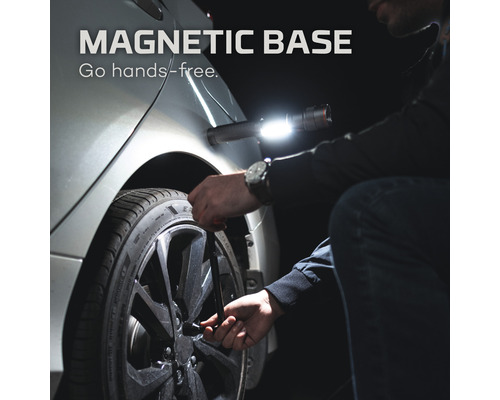 Mann wechselt mit Schraubenschlüssel einen Reifen, wobei eine magnetische LED-Lampe am Auto befestigt ist