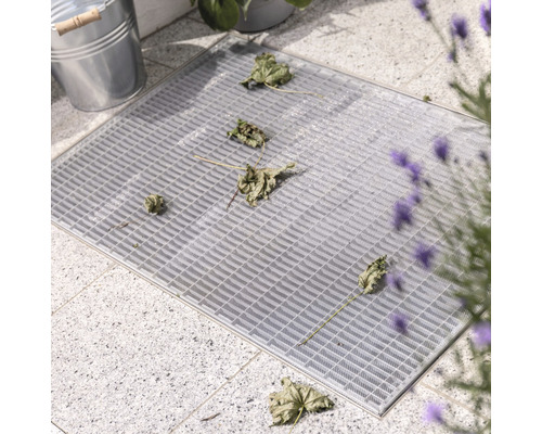 Grauer Gitterrost mit Laub auf Pflastersteinen