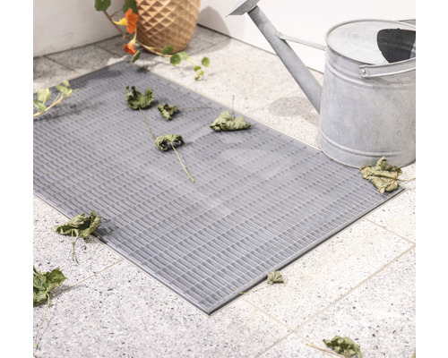 Grauer Fussabtreter aus Gitterstruktur mit Blumenvase und Giesskanne