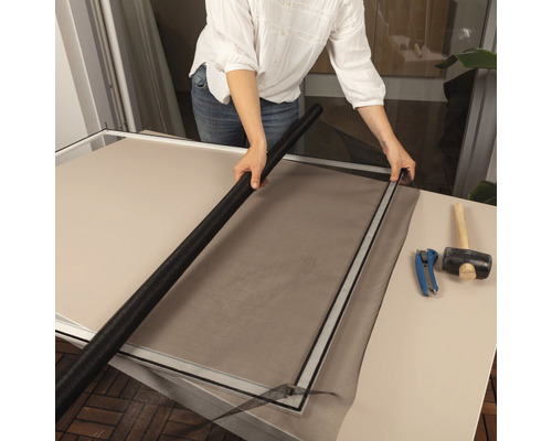 Une personne installe une moustiquaire dans un cadre avec des outils sur une table.