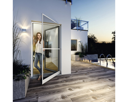 Scène avec une femme debout dans la porte moustiquaire ouverte d''une maison, donnant sur une terrasse avec piscine.