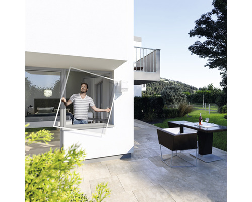 Un homme fixe une moustiquaire à une fenêtre d''une maison avec des meubles de jardin.