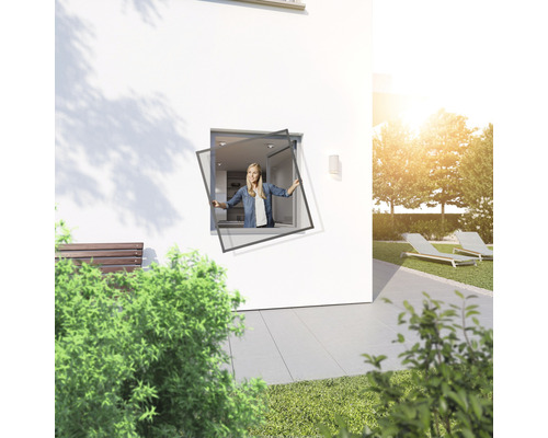 Femme installe une moustiquaire sur la fenêtre d''une maison avec jardin