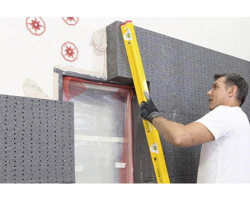 Un homme utilise un niveau à bulle pour fixer un panneau isolant en polystyrène sur un mur de maison.