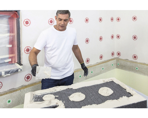 Homme enduisant une plaque isolante sur un mur intérieur avec du mortier