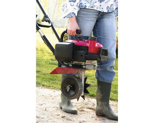 Frau trägt eine Motorhacke im Garten.
