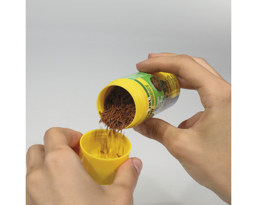 Hände füllen Insektenfutter von JBL in einen gelben Deckel