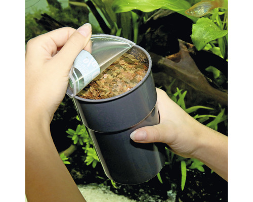 Une personne ouvre une boîte de nourriture pour poissons devant un aquarium