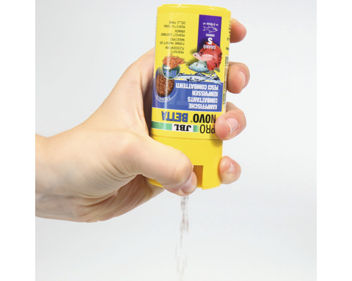 Eine Hand schüttet JBL Pro Novo Betta Fischfutter aus einer gelben Dose.