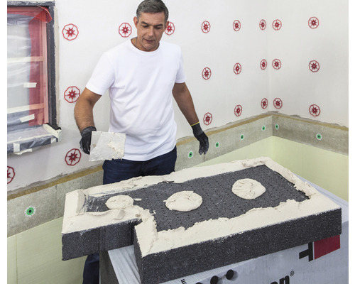 Mann trägt Dämmstoffkleber auf eine Dämmplatte auf. Dämmstoffplatten werden an einer Wand mit Dämmstoffdübel befestigt.