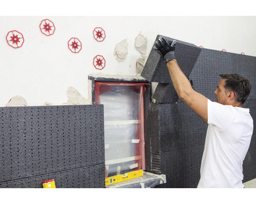 Mann befestigt Dämmplatten an einer Wand neben einem Fenster zur Wärmedämmung.