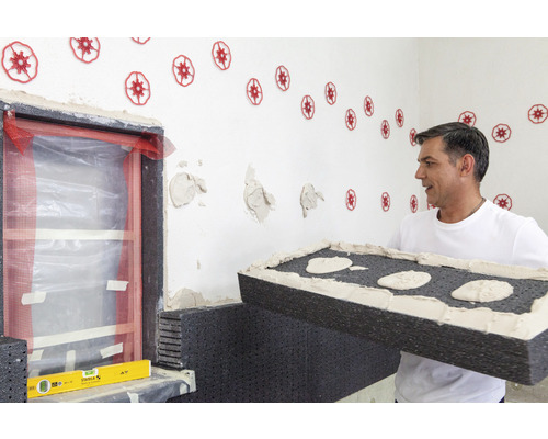 Un artisan fixe des panneaux isolants sur un mur de maison
