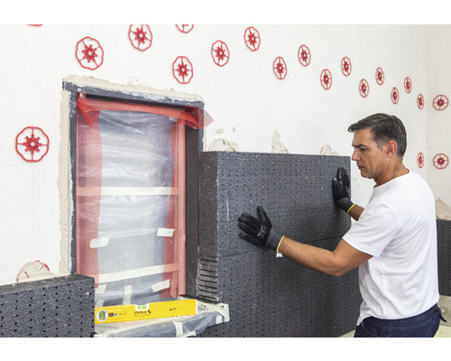 Un homme fixe des panneaux d''isolation thermique sur le mur à côté d''une fenêtre. Des chevilles d''isolation sont fixées au mur.