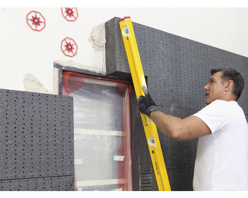 Un homme utilise un niveau à bulle pour installer une isolation thermique sur un mur de maison.