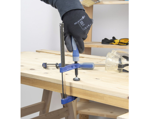 Eine Person befestigt ein Werkstück mit einer Schraubzwinge auf einer Holzoberfläche.