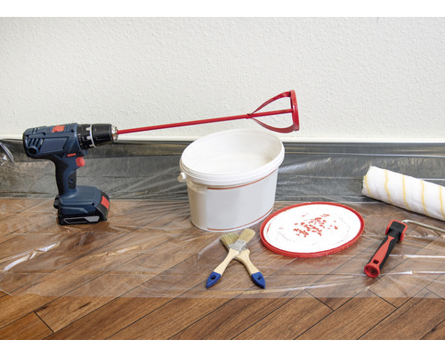 Scène avec perceuse, mélangeur de peinture, pot de peinture, pinceaux et rouleau à peinture sur une feuille de protection