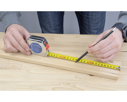 Une personne mesure une planche de bois avec un mètre ruban et la marque avec un crayon.