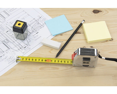 Plan de construction avec crayon, taille-crayon, gomme, notes adhésives et mètre ruban sur une table en bois
