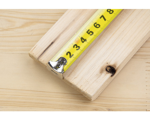 Un mètre ruban jaune mesure une planche de bois.