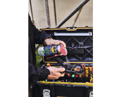 Eine Person sprüht mit WD-40 Spezialist Kontaktspray eine Zange vor einem Werkzeugkasten ein.