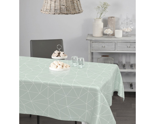 Table à manger avec une nappe vert clair et un motif géométrique dans une pièce lumineuse.