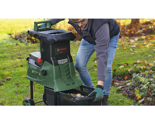 Gartenszene mit einem Mann, der einen Häcksler bedient und einen Fangkorb entleert. Bosch Logo.