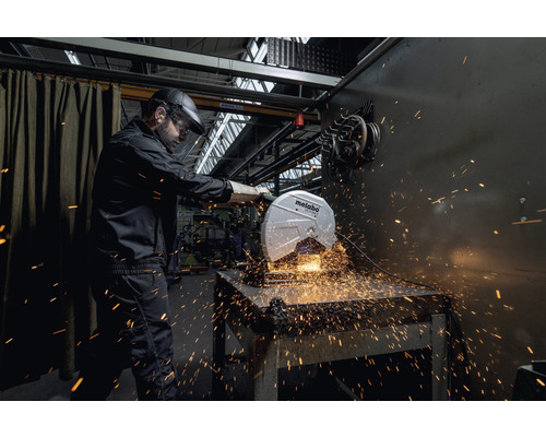 Un homme portant un casque et des lunettes de protection utilise une machine à tronçonner Metabo pour couper du métal, des étincelles jaillissent.