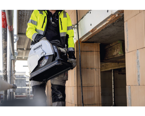 Un ouvrier du bâtiment transporte une scie à tronçonner les métaux Metabo CS 23-355 S sur un chantier.