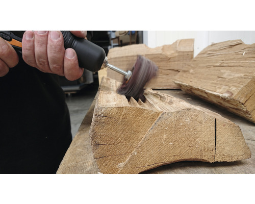 Une personne utilise une brosse rotative pour travailler une pièce de bois.