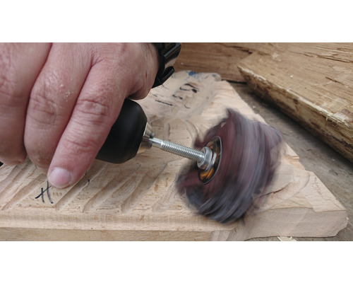 Une personne ponce du bois avec une brosse rotative et un outil.